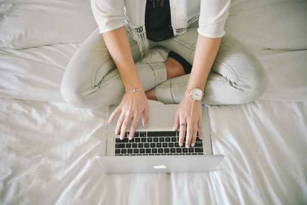 Donna che scrive sul letto con computer con le gambe incrociate